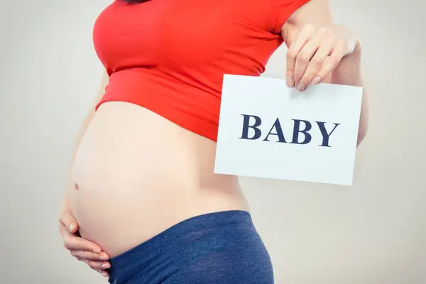 Pregnant Woman Holding White Card Inscription Baby Expecting Birth Newborn lizenzfreie Stockfotos