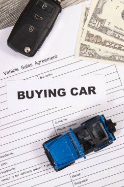 Küçük mavi oyuncak araba, siyah anahtar, dolar banknotları ve bir çeşit araç satış anlaşması. Araba satın alma yazıtları. Satışlar ve yeni ya da kullanılmış araba alımları