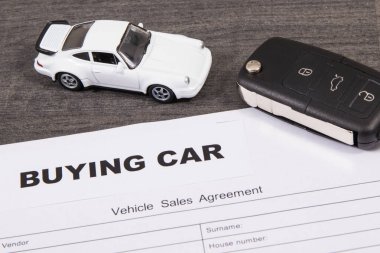 Küçük beyaz oyuncak araba, siyah araba anahtarı ve araç satış sözleşmesi. Araba satın alma yazıtları. Araba satışı ya da alımları. Ulaşım