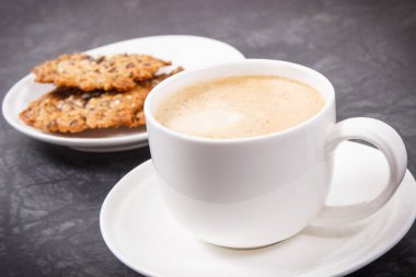 Sütlü kahve ve ballı ev yapımı yulaf ezmesi kurabiyeleri ve beyaz tabakta farklı sağlıklı tohumlar. Lezzetli çıtır tatlı.