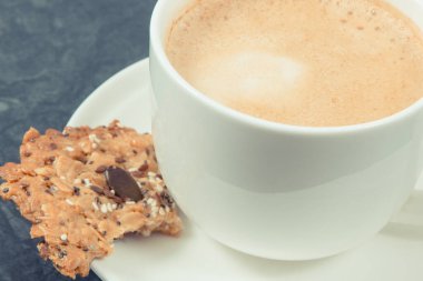 Bir fincan kahve ve ballı taze ev yapımı yulaf ezmesi kurabiyeleri ve farklı sağlıklı tohumlar. Lezzetli çıtır tatlı.