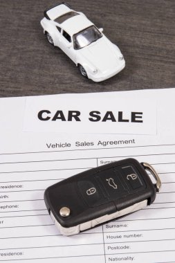 Küçük beyaz oyuncak araba, siyah araba anahtarı ve araç satış sözleşmesi. Araba satışı. Araba satışı ya da alımları. Ulaşım