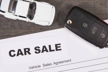 Küçük beyaz oyuncak araba, siyah araba anahtarı ve araç satış sözleşmesi. Araba satışı. Satışlar ya da alımlar yeni ya da kullanılmış araçlar. Ulaşım