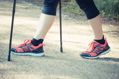 Spor ayakkabılı yaşlı kadın bacakları İskandinav yürüyüşü yapıyor. Yaşlılıkta sağlıklı spor yaşam tarzları