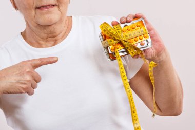 Elinde vitamin paketleri, takviyeler ve santimetre ile yaşlı bir kadın. Tedavi, zayıflama veya yaşlılıkta bağışıklığı güçlendirme. Sağlık hizmetleri