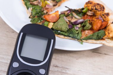 Glukometre, taze pişmiş vejetaryen pizzayla şeker seviyesini ölçmek ve kontrol etmek için kullanılır. Diyabet konsepti sırasında besin