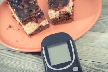 Şeker seviyesini ölçmek için kullanılan glikoz ölçer ve kirazlı ve çikolatalı fırında pişmiş cheesecake parçaları. Diyabet konsepti sırasında besin