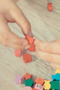 Küçük çocuğun elleri iplikten ve renkli boncuklardan bilezik yapıyor. Çocukların motor becerilerinin, koordinasyonun, yaratıcılığın ve mantıksal düşüncenin geliştirilmesi