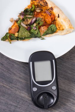 Glukometre, taze pişmiş vejetaryen pizzayla şeker seviyesini ölçmek ve kontrol etmek için kullanılır. Diyabet konsepti sırasında besin