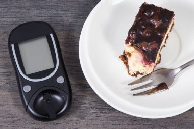Şeker seviyesini ölçmek için kullanılan glikoz ölçer ve kirazlı ve çikolatalı cheesecake parçaları. Diyabet konsepti sırasında besin