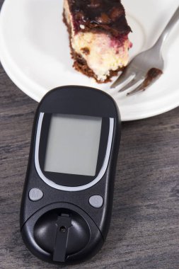 Şeker seviyesini ölçmek için kullanılan glikoz ölçer ve kirazlı ve çikolatalı cheesecake parçaları. Diyabet konsepti sırasında besin