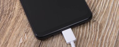 Siyah akıllı telefon ve bağlı beyaz şarj kablosu. Cep telefonu şarj ediliyor