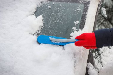 Araba ve ön camlardan kar temizleyen bir kadın eli. Ulaşım sırasında kış sorunları