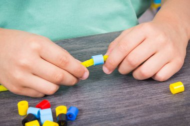 Yaratıcı sopaları ve bilezik yapımında kullanılan renkli boncukları olan anaokulu öğrencilerinin elleri. Çocukların motor becerilerinin, koordinasyonun, yaratıcılığın ve mantıksal düşüncenin geliştirilmesi