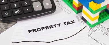 Renkli oyuncak blokları, hesap makinesi ve artan emlak vergisi artışlarını gösteren grafiklerden oluşan küçük bir ev. Hesaplama ve vergi ödeme