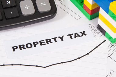 Renkli oyuncak blokları, hesap makinesi ve artan emlak vergisi artışlarını gösteren grafiklerden oluşan küçük bir ev. Hesaplama ve vergi ödeme