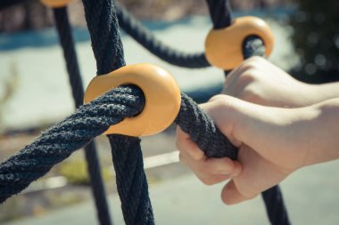 Küçük anaokulu çocuğu elleri ve yaz parkında oyun parkına tırmanmak için siyah ip. Çocuk gelişimi kavramı