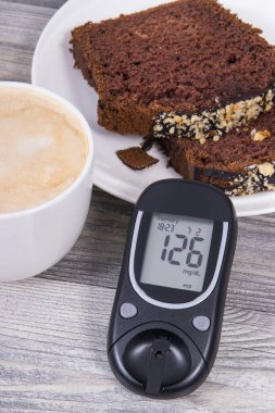 Şekerin ölçülmesi sonucu glikoz ölçer, çikolatalı tatlı kek ve sütlü kahve. Diyabet sırasında şeker seviyesini ölçmek ve kontrol etmek