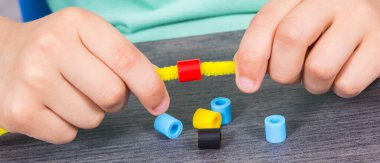 Yaratıcı sopaları ve bilezik yapımında kullanılan renkli boncukları olan anaokulu öğrencilerinin elleri. Çocukların motor becerilerinin, koordinasyonun, yaratıcılığın ve mantıksal düşüncenin geliştirilmesi