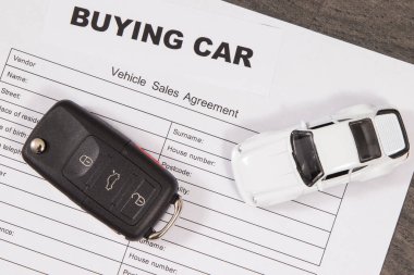 Küçük beyaz oyuncak araba, siyah araba anahtarı ve araç satış sözleşmesi. Araba satın alma yazıtları. Araba satışı ya da alımları. Ulaşım