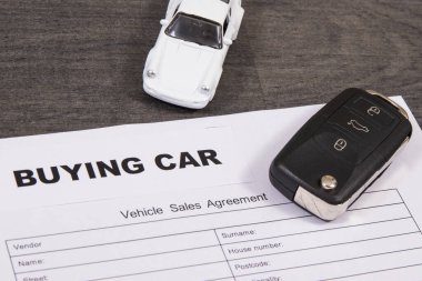 Küçük beyaz oyuncak araba, siyah araba anahtarı ve bir çeşit araç satış anlaşması. Araba satın alma yazıtları. Satışlar ya da alımlar yeni ya da kullanılmış araçlar. Ulaşım