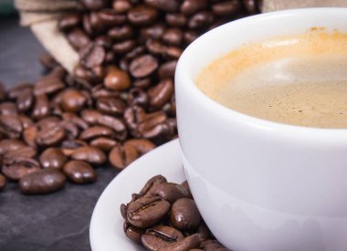 Beyaz cam bardakta kahve ve kavrulmuş kahve çekirdekleri.