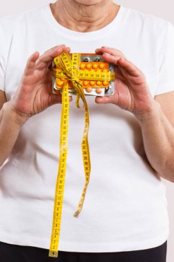 Elinde vitamin paketleri, takviyeler ve santimetre ile yaşlı bir kadın. Tedavi, zayıflama veya yaşlılıkta bağışıklığı güçlendirme. Sağlık hizmetleri