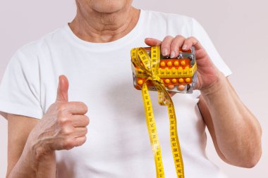 Elinde vitamin paketleri, takviyeler ve santimetre ile yaşlı bir kadın. Tedavi, zayıflama veya yaşlılıkta bağışıklığı güçlendirme. Sağlık hizmetleri