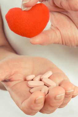Tabletleri, vitaminleri, takviyeleri ve kırmızı kalbi olan yaşlı bir kadının eli. Tedavi ya da yaşlılıkta bağışıklığın güçlendirilmesi. Sağlık hizmetleri