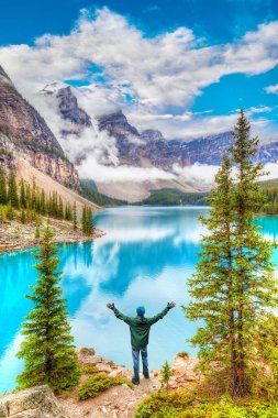 Moraine Gölü 'nde silahlı bir yürüyüşçü. Alçak bulutlar Banff Ulusal Parkı' nın Kanada Dağları 'ndaki Ten Peaks Vadisi' ne doğru inerken. Dikey yönelim.