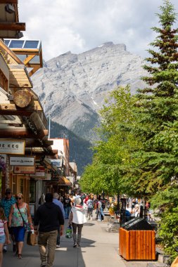 BANFF, CanADA - 5 Temmuz 2023: Banff Ulusal Parkı 'ndaki Kasırga Dağı' nın arka planında Banff 'ın tadını çıkaran turistler. Kasaba, dağlık çevresi ve kaplıcalarıyla ünlü büyük bir Kanada turizm beldesi..