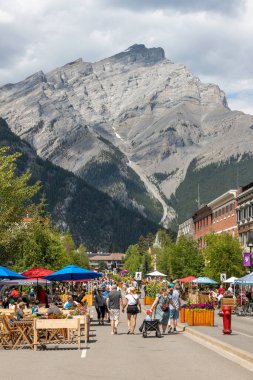 BANFF, CanADA - 5 Temmuz 2023: Banff Ulusal Parkı 'ndaki Kasırga Dağı' nın arka planında Banff 'ın tadını çıkaran turistler. Kasaba, dağlık çevresi ve kaplıcalarıyla ünlü büyük bir Kanada turizm beldesi..