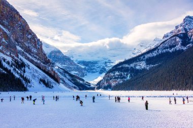 Unidentifiable visitors skating on frozen Lake Louise in the winter against the backdrop of the stunning Victoria Glacier. The iconic Lake Louise typically freezes from November to mid-April and draws visitors from all over the world during Winter. clipart