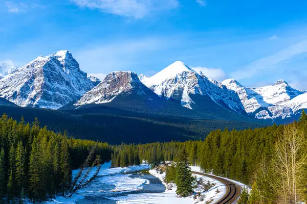 加拿大洛基山脉冬季的莫朗特曲线 其特色是雪覆的哈德多峰 费尔维山 怀特山和尼布克山 一条铁路在前景中蜿蜒穿过风景 免版税图库图片