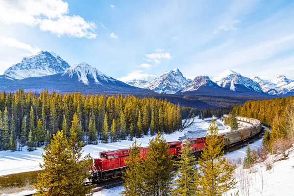 红色货运列车通过班夫国家公园内的博山谷的莫兰特弯道 艾伯塔省加拿大岩石上美丽的冬季雪景 背景为圣殿山 图库照片