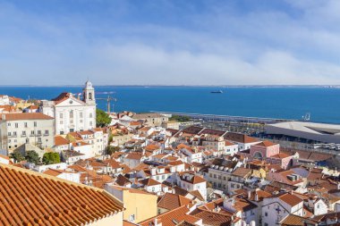 Portekiz, Lizbon 'daki Miradouro de Santa Luzia bakış açısından görüldüğü üzere, Tagus Nehri boyunca uzanan kırmızı çatılı, renkli evleri ile eski Alfama bölgesinin silueti.