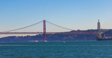 25 de Abril Köprüsü 'nün panoraması ya da Lizbon' daki Tagus Nehri 'nin karşısındaki 25 Nisan Köprüsü. Gün batımında şehrin simgesine parlayan güneş ve arka plandaki Kral İsa heykeli.. 