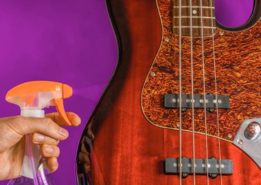 Hand holding a a cleaning spray before a bass guitar body, guitar care concept clipart