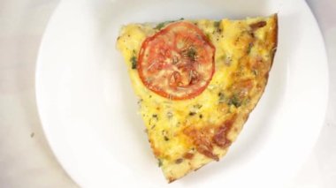 Kırsal bir ahşap tahta üzerine yerleştirilmiş, altın, pullu bir hamurlu, fırında pişirilmiş nefis bir kiş turtasının yakından görüntüsü. Dolgusunda görünür sebzeler ve erimiş peynir yer alıyor.