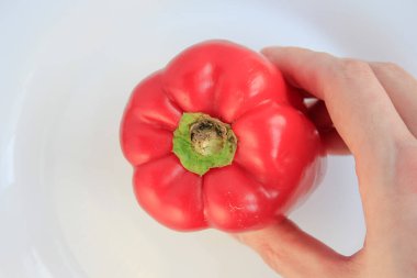  Bir insanın eli beyaz bir yüzey üzerinde canlı kırmızı bir dolma biber tutuyor, şeklini ve rengini vurguluyor.