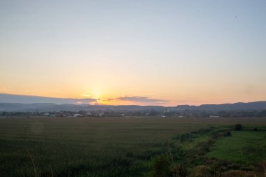 Kırsal bir arazide, canlı bir gökyüzü, tarlaları ve uzak bir köyü olan manzaralı bir gün doğumu..