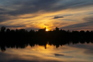 Infernal sunset behind trees and reflection in water.