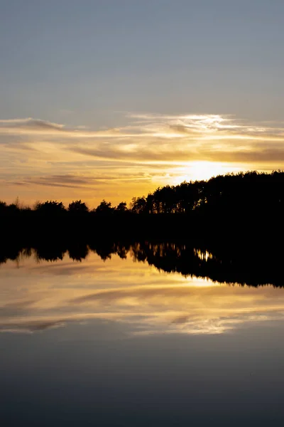 stock image Atmospheric sunset behind trees and reflection in water.