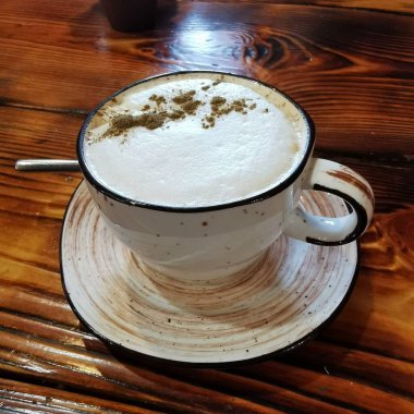 a cup of coffee on a wooden table with foam and cinnamon