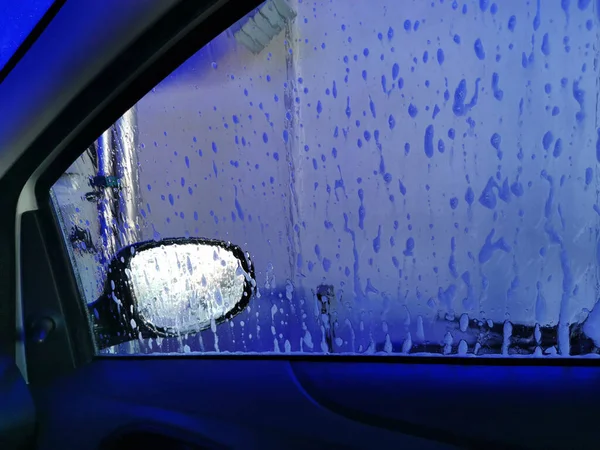 Car Care Business. Automatic Car Wash Process. Spray foam bubble shampoo on the car surface. View inside the car salon