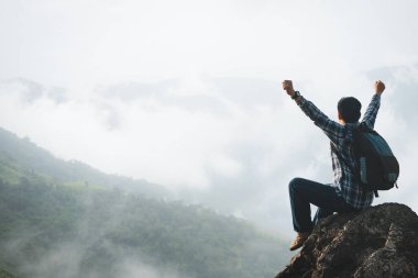 Sırt çantası taşıyan başarılı bir gezgin sisli bir günde dağın tepesinde oturur. Macera yolculuğu ve başarı konsepti.