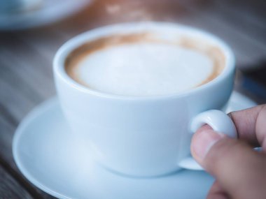 Erkek eli beyaz bir kahve fincanı tutuyor ve arka planda sigara içiyor.