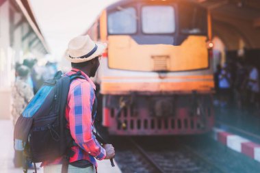 Sırt çantalı, sırt çantalı ve şapkalı Afrikalı bir adam tren istasyonunda gezginlerle seyahat ediyor. Tren istasyonunda yürüyen bir gezgin.