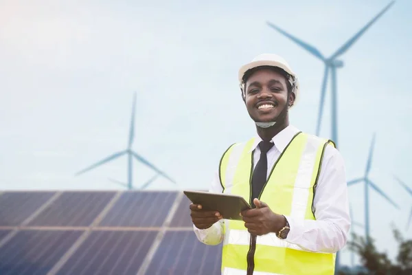 African engineer manager stand  front solar photovoltaic and wind turbines generating electricity power station.