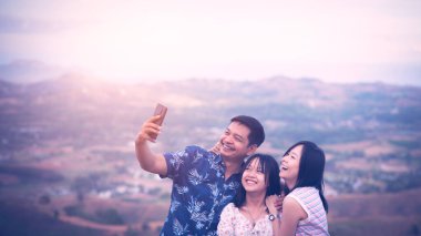 Mutlu bir aile elinde akıllı telefon fotoğrafı tutuyor. Güzel bir dağ manzarası geçmişi var.